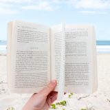 海辺の砂浜で本を広げている画像